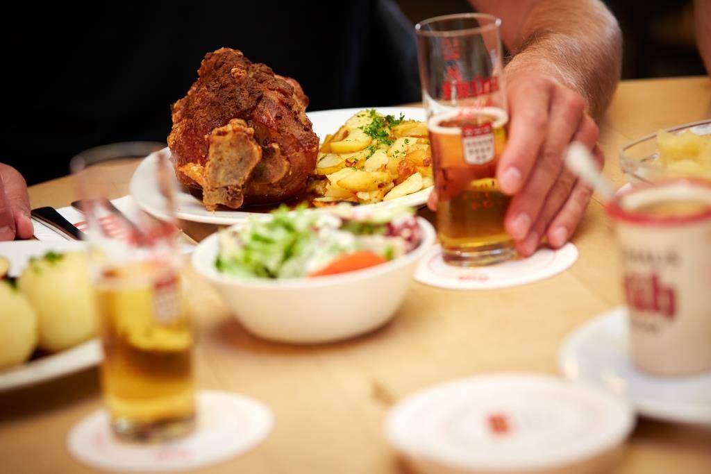 man holding glass of kolsch next to a delicious food spread