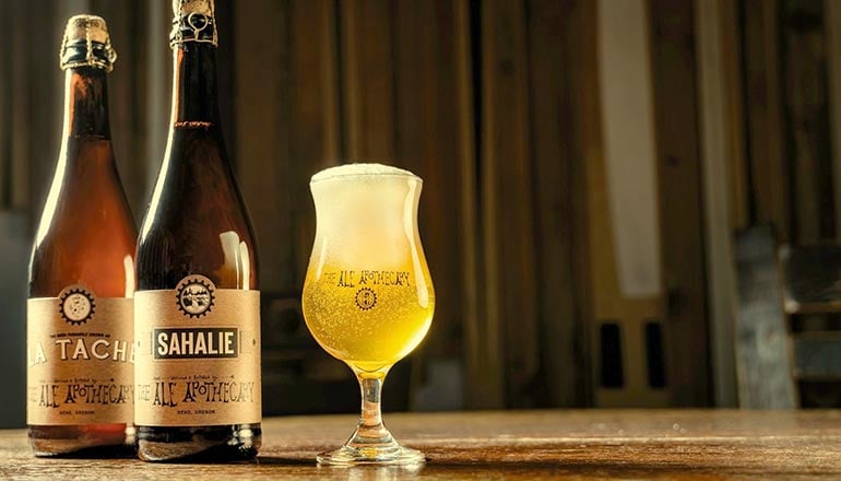 ale apothecary beer bottles with a tulip glass full of saison sitting beside them