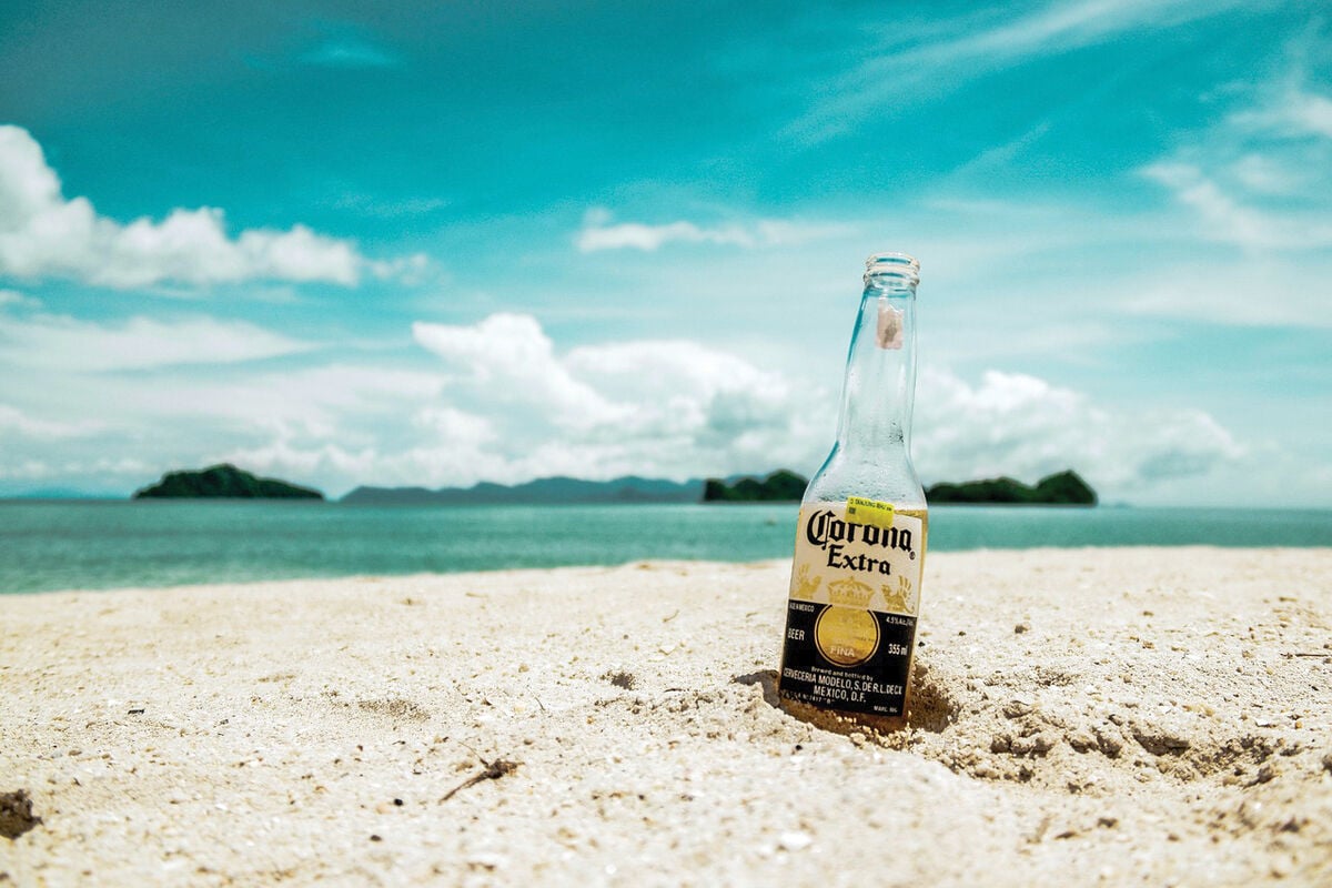 Bottle of Corona Extra in the sand along side a beach.