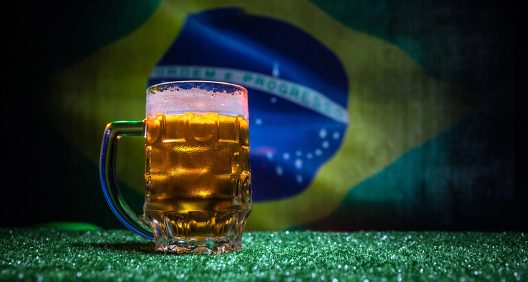 A glass of beer on a green surface with the Brazilian flag in the background