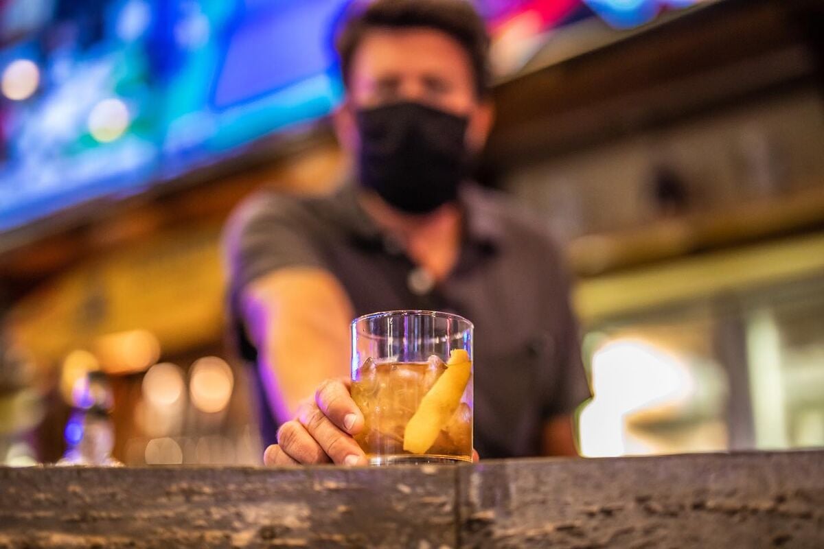 bartender wearing mask proffers a drink at the bar