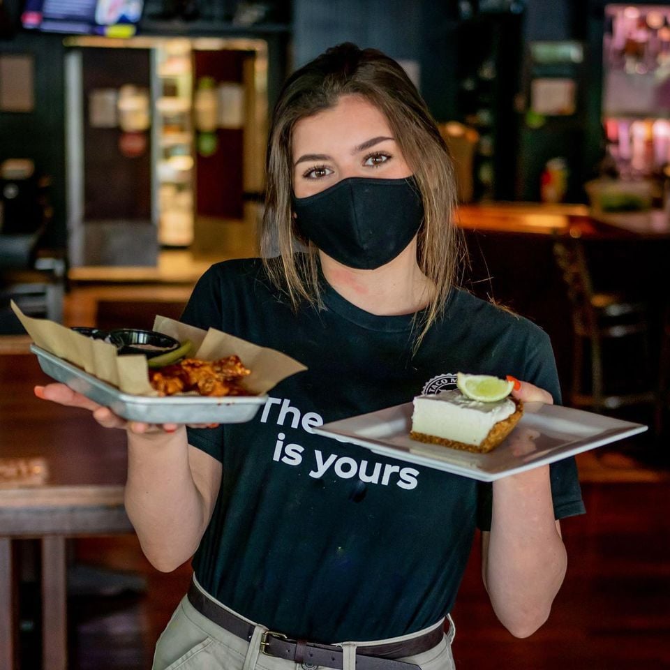 server wearing a mask carries two trays of food
