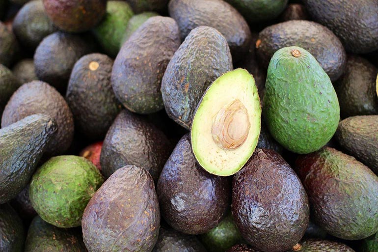 pile of avocados with one halved on top
