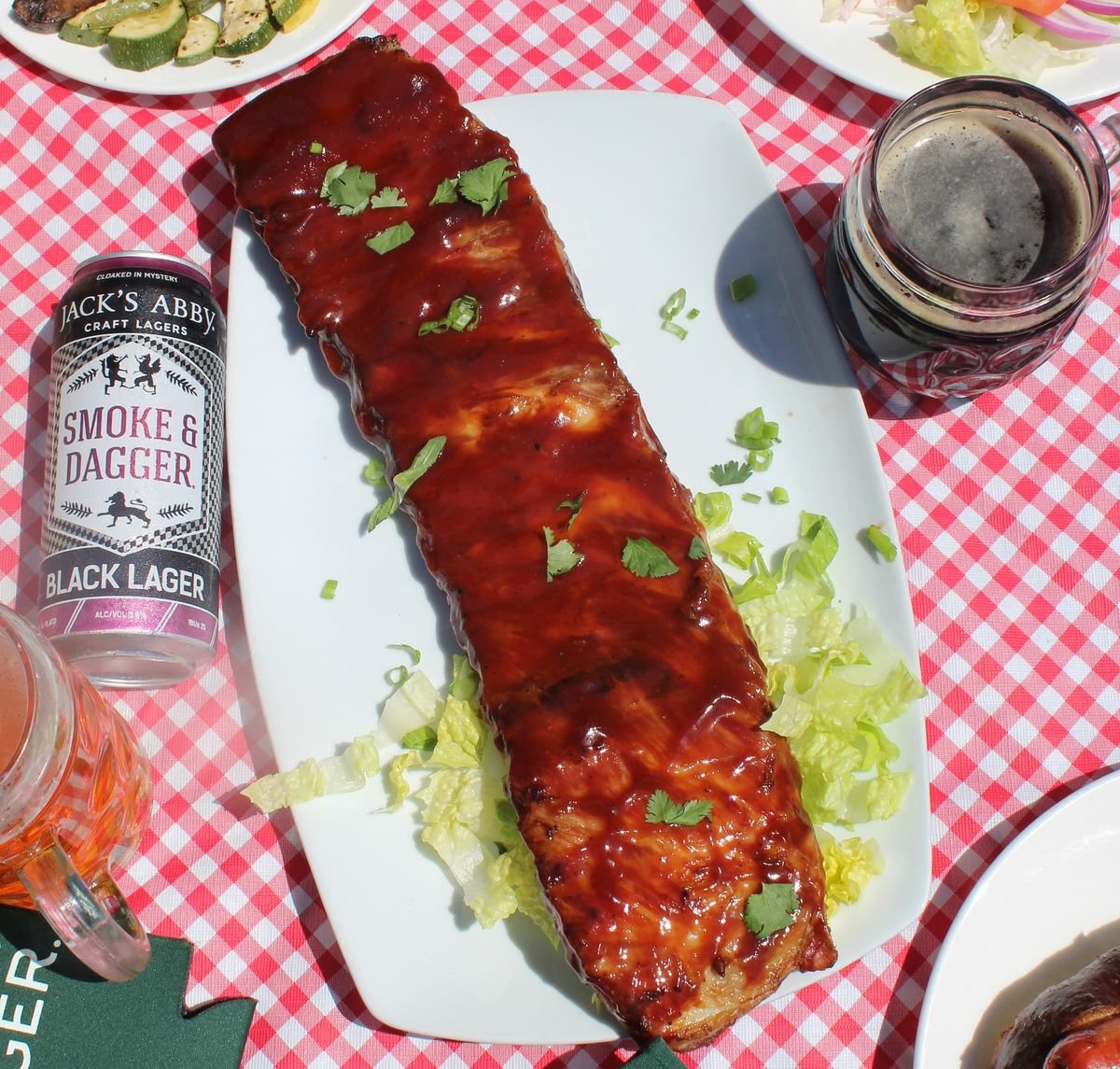 Plate of barbecue ribs with a can and poured mug of Jack' Abbey Smoke & Dagger Black Lager