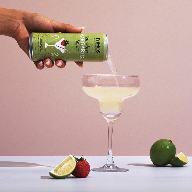 pamos thc cocktails being poured into glassware next to strawberries and limes