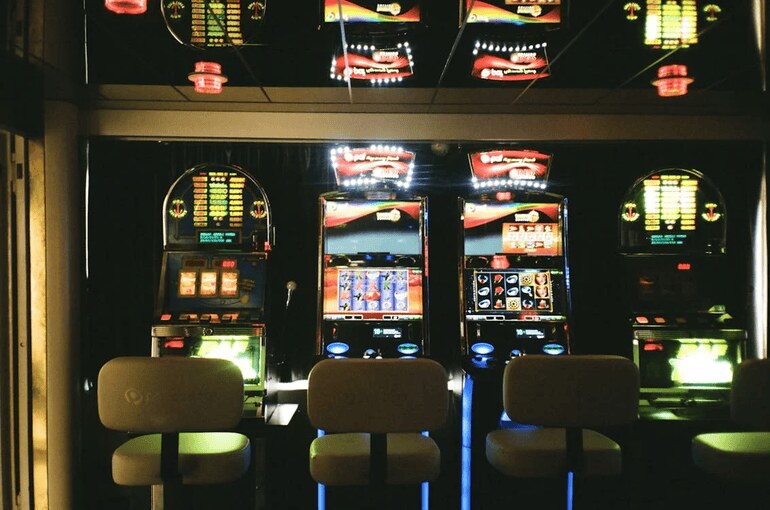 Slot machines in a dimly lit casino with glowing screens and a reflective ceiling