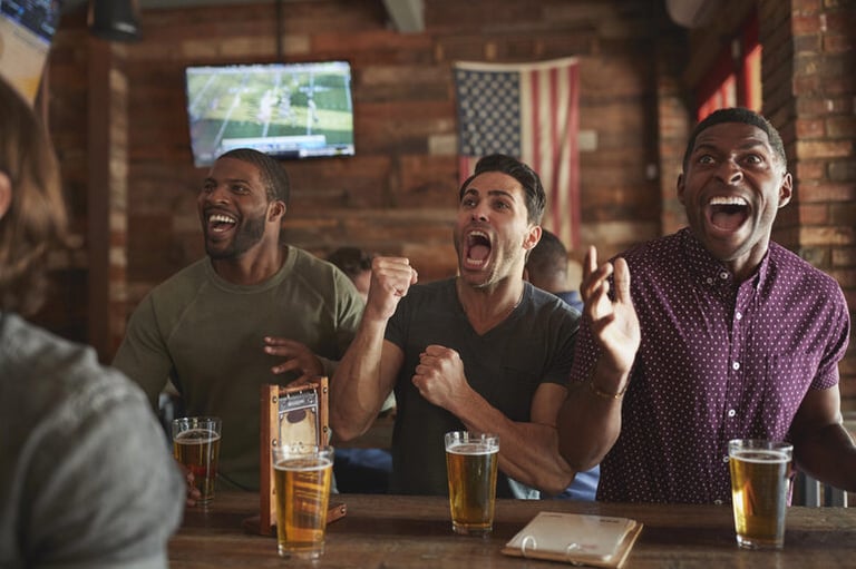 Excited friends enjoying beer while watching a sports game at a bar