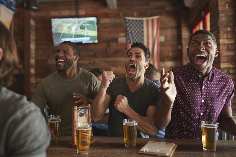 Excited friends enjoying beer while watching a sports game at a bar