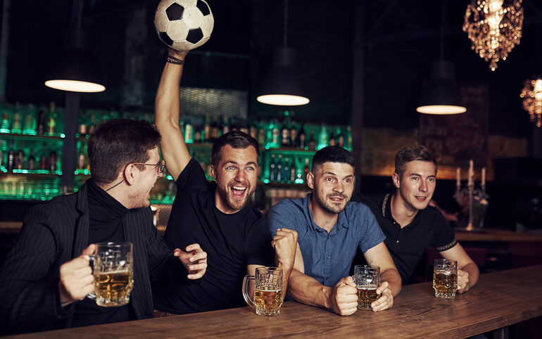 Sports fans in a bar watching football and holding beer in their hands