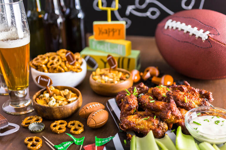 A glass of beer and a plate of game-day snacks on a table with an American football