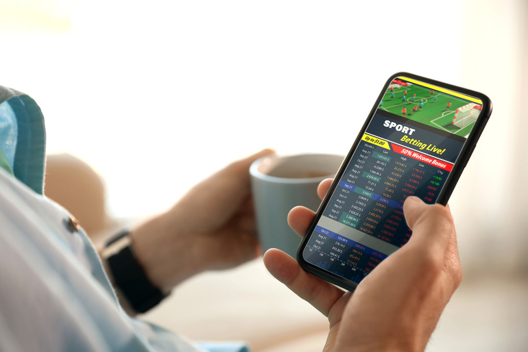 A man holding a cup of tea in one hand and placing live sports bets on the 888Starz app