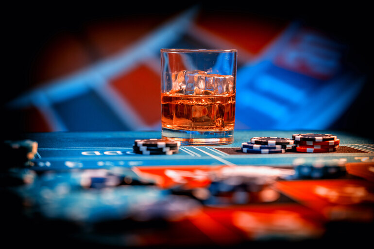 A glass of fine whiskey with ice on a casino table surrounded by poker chips