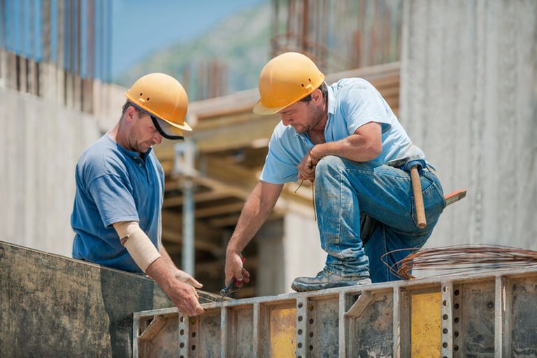 Two construction workers are installing concrete formwork frames