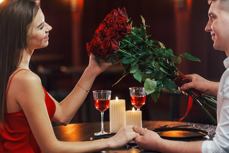 Couple enjoying a romantic date with roses, candles, and drinks in a cozy setting