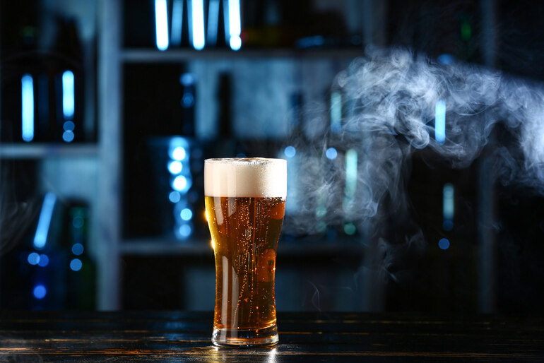A glass of fresh beer with visible carbon dioxide bubbles on a bar table