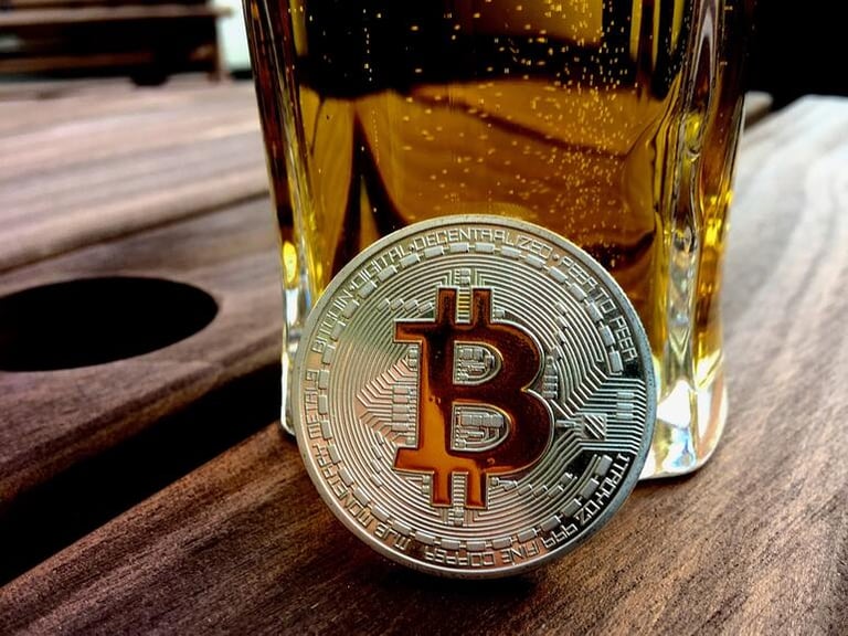 A cryptocurrency coin, Bitcoin, beside a glass of beer