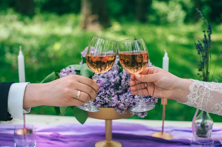 Bride and groom clinking glasses of sparkling rosé at an outdoor wedding celebration