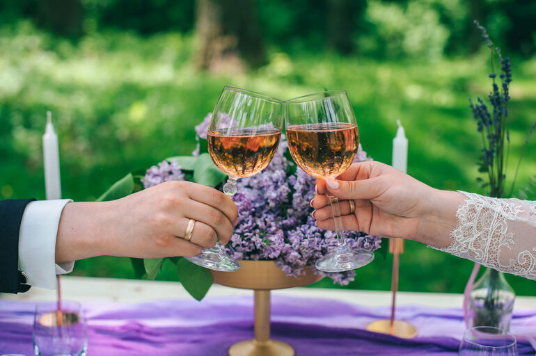 Bride and groom clinking glasses of sparkling rosé at an outdoor wedding celebration
