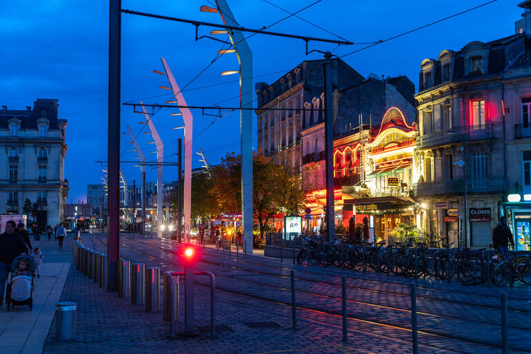 Evening street view in Brussels featuring illuminated buildings, vibrant nightlife, tram lines, and people strolling along the sidewalk