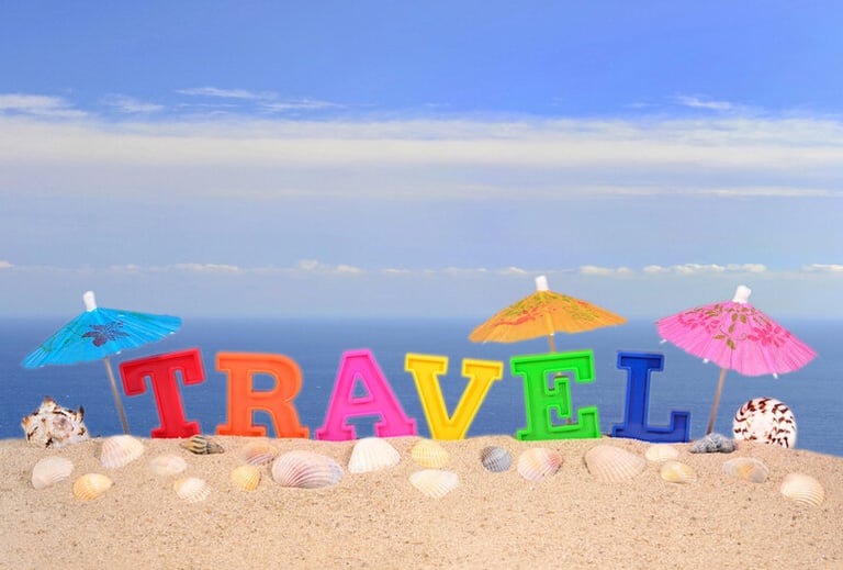 Colorful TRAVEL letters on a sandy beach with seashells, paper umbrellas, and a clear blue sky in the background