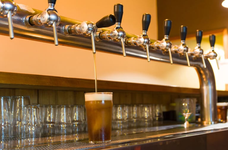 A row of beer taps pouring a pint at a brewpub bar