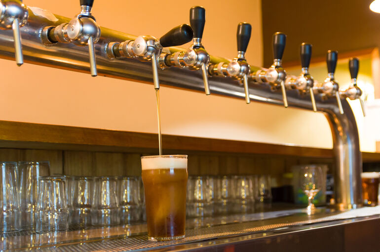 A row of beer taps pouring a pint at a brewpub bar
