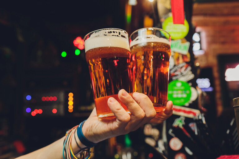 Close-up of a hand holding two pints of beer in a lively bar setting