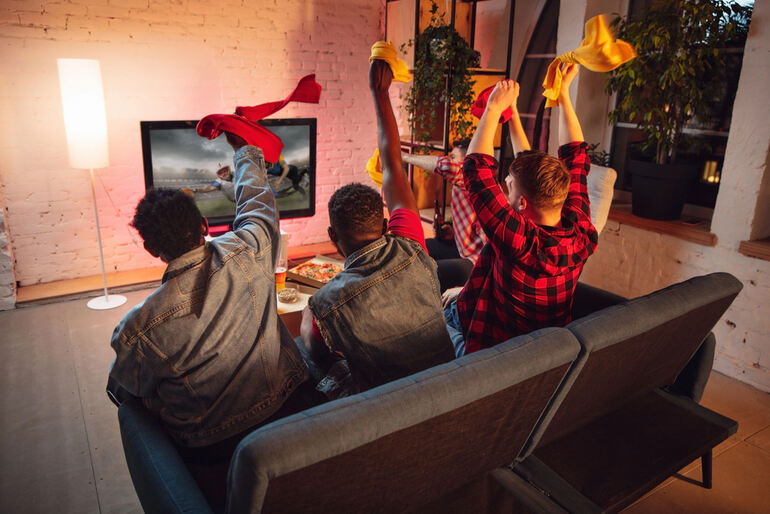 A group of four friends enthusiastically watching a sports game and enjoying beers