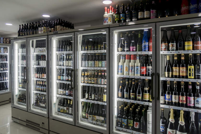 A well-lit commercial beer refrigerator stocked with a wide variety of bottled craft beers