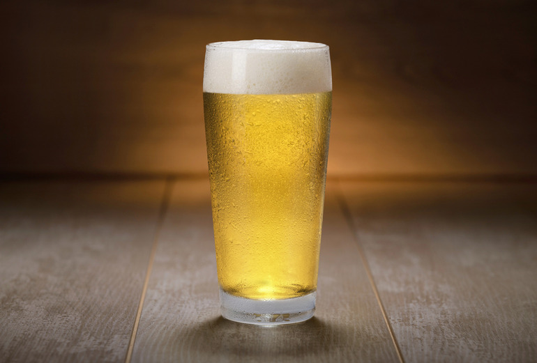 A chilled pint glass of indian pale ale with a foamy head placed on a wooden surface