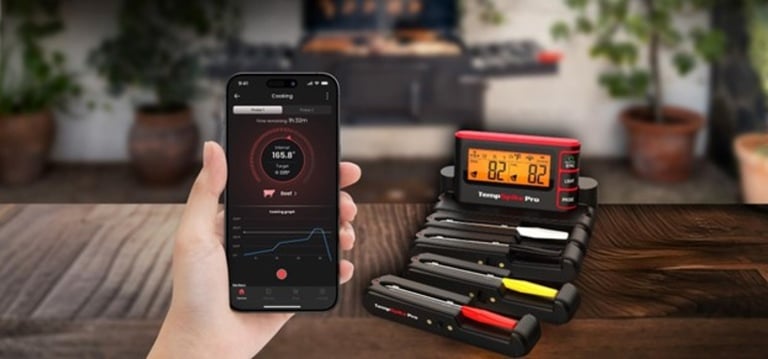 Hand holding a smartphone displaying real-time meat temperature readings via app