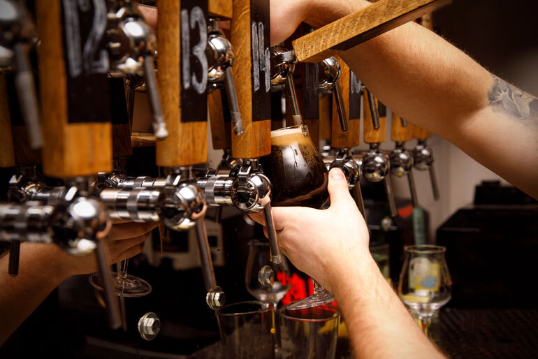 A beer lover is pouring a dark craft beer from a tap in a modern taproom