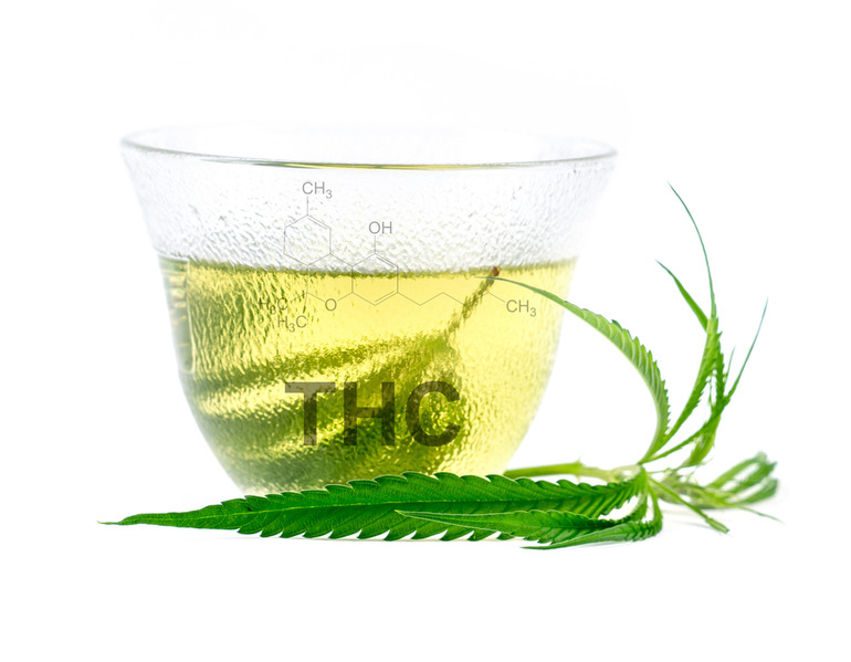 A clear glass cup filled with a light green THC-infused drink