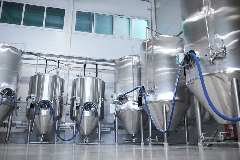 Large stainless steel fermenters connected with hoses inside a brewery for functional beer production