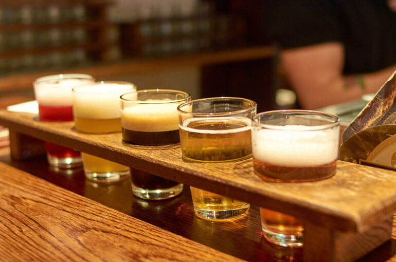 A wooden flight board with five small glasses of the best session beers arranged for tasting.