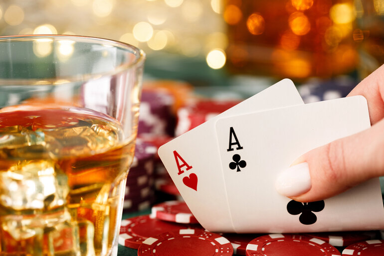 Player holding pocket aces at a casino poker table with a beer glass and poker chips, celebrating a big jackpot win at Pinco Casino.