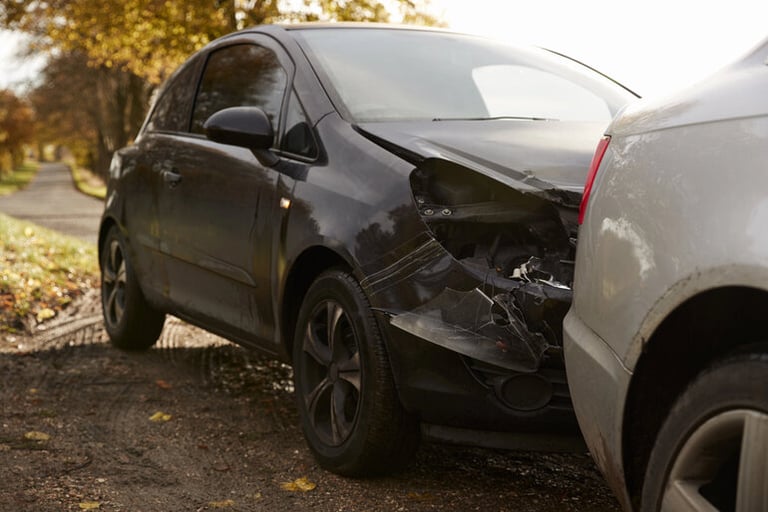 A black car with front-end damage after a rear-end collision with a white vehicle on a rural road