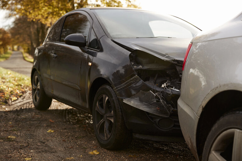 A black car with front-end damage after a rear-end collision with a white vehicle on a rural road