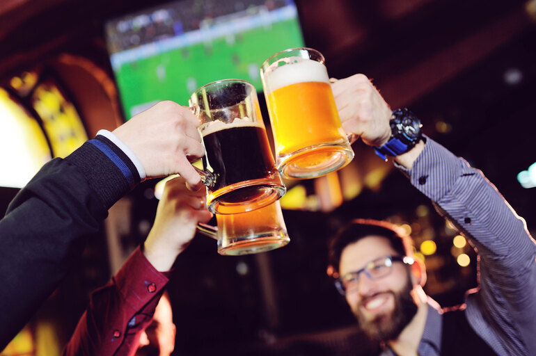 Friends clinking beer mugs while watching a sports match in a bar