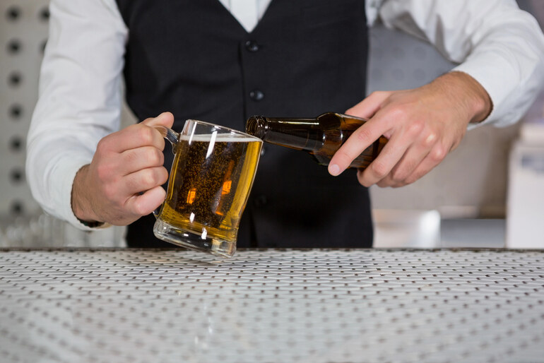 Bartender pouring beer from a bottle into a glass mug at a bar counter