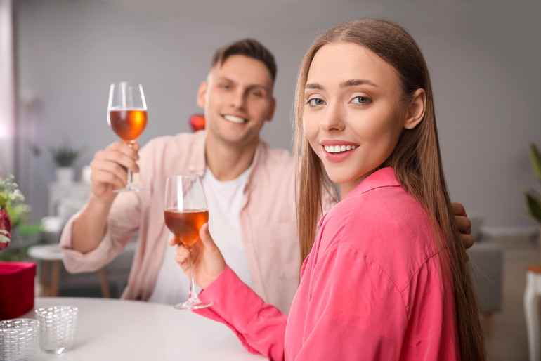 Two people on a date smiling and raising glasses of beer at a cozy table.