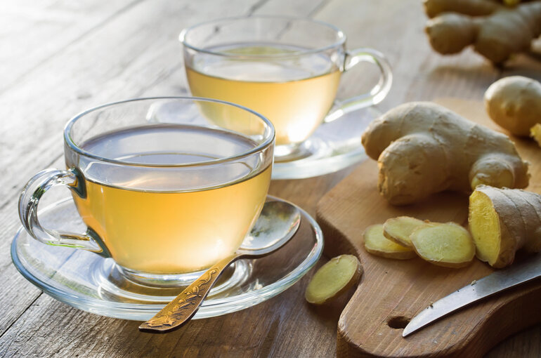 Two cups of ginger tea on a wooden table with fresh ginger root and slices, a natural food that helps relieve menopause symptoms
