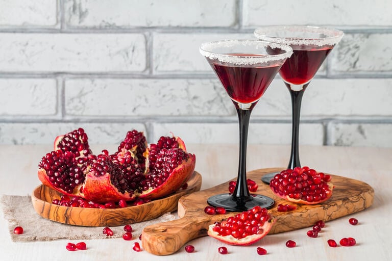 Two pomegranate cocktails in elegant glasses with fresh pomegranate seeds and fruit on a wooden board, perfect for dessert-inspired home mixology.