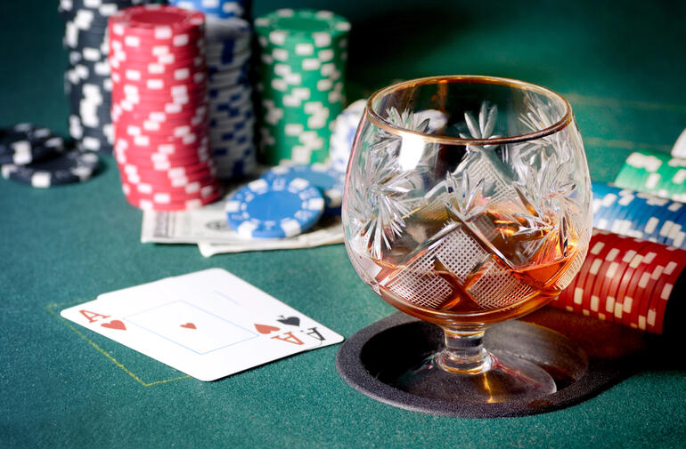 A glass of liquor on a casino table beside poker chips, money, and playing cards, illustrating responsible gambling and drinking.