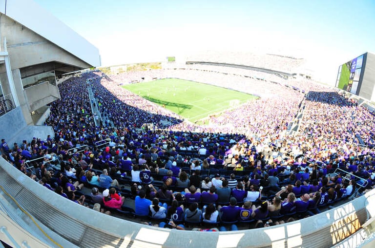 Full stadium crowd wearing purple during a soccer match, study on declining home field advantage since the 1990s.