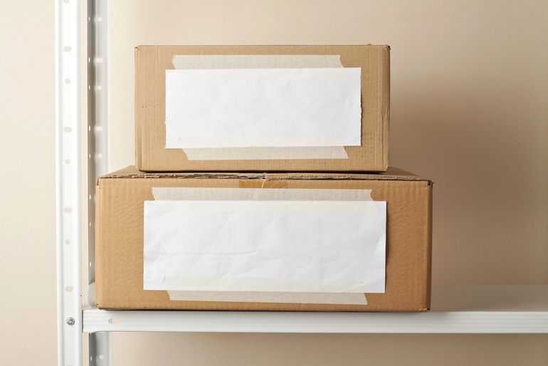 Stacked cardboard storage boxes with blank labels on a shelf, highlighting how proper packaging protects inventory