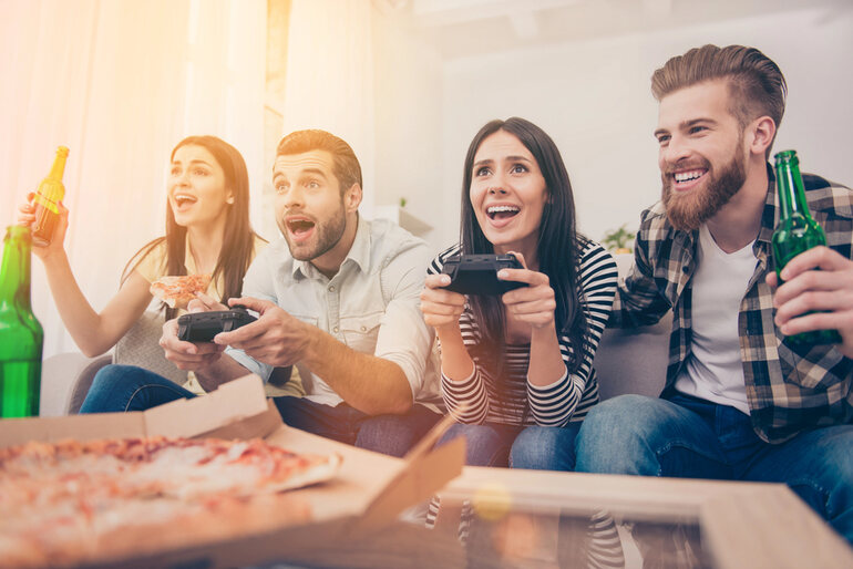 A group of friends drinking beer, eating pizza, and playing video games during a casual beer game night.