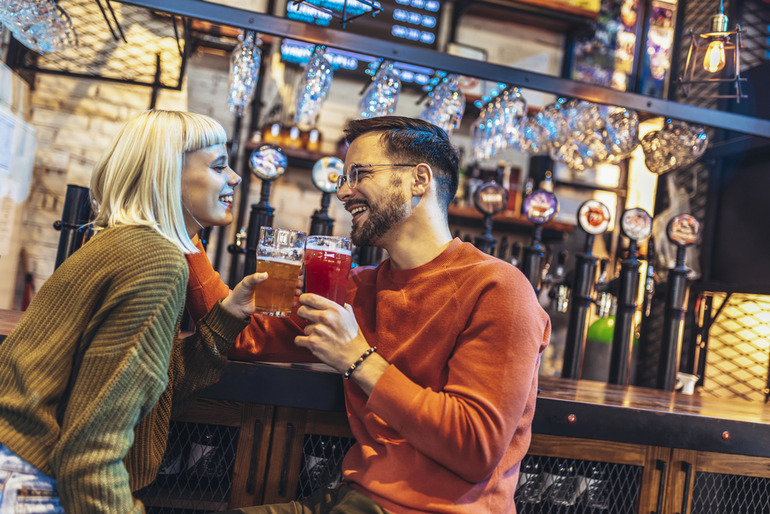 A man and a woman enjoying a relaxed brewery date night while clinking beer glasses at a cozy table.