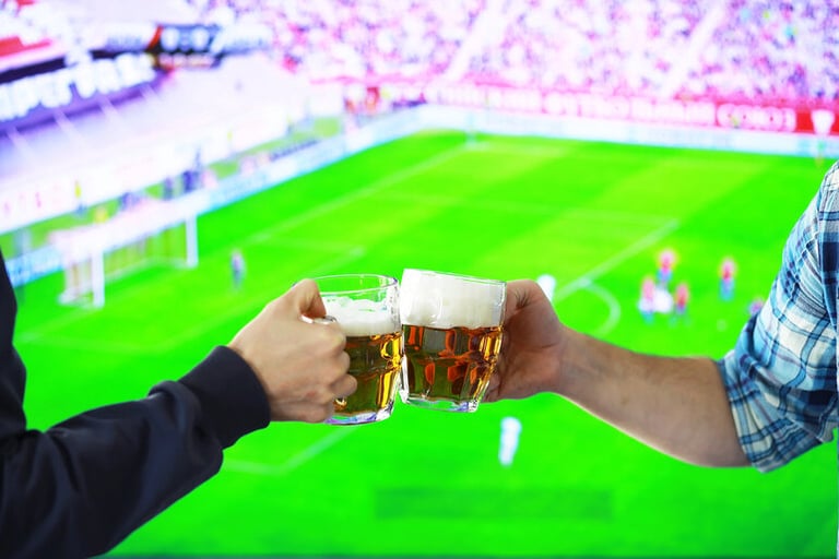 A couple clinking beer mugs during a football match, highlighting global matchday traditions.
