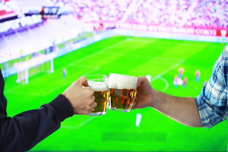 A couple clinking beer mugs during a football match, highlighting global matchday traditions.